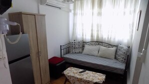 Une petite chambre comprenant un lit, une petite table, une armoire et un réfrigérateur.