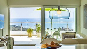 Een moderne keuken met een groot raam met uitzicht op zee, een eethoek met een tafel en stoelen, en een blik op de kustlijn.