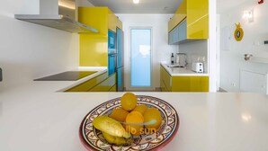 Een moderne keuken met gele kastjes, een roestvrijstalen afzuigkap en een centraal keukenblok met een fruitschaal.
