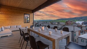 Una terraza de madera con una mesa lista para comer, un sofá y sillas.