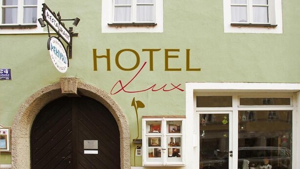 A hotel with a large arched entrance, a signboard above the door, and a window display with various items. - Hotel Lux (Regensburg)
