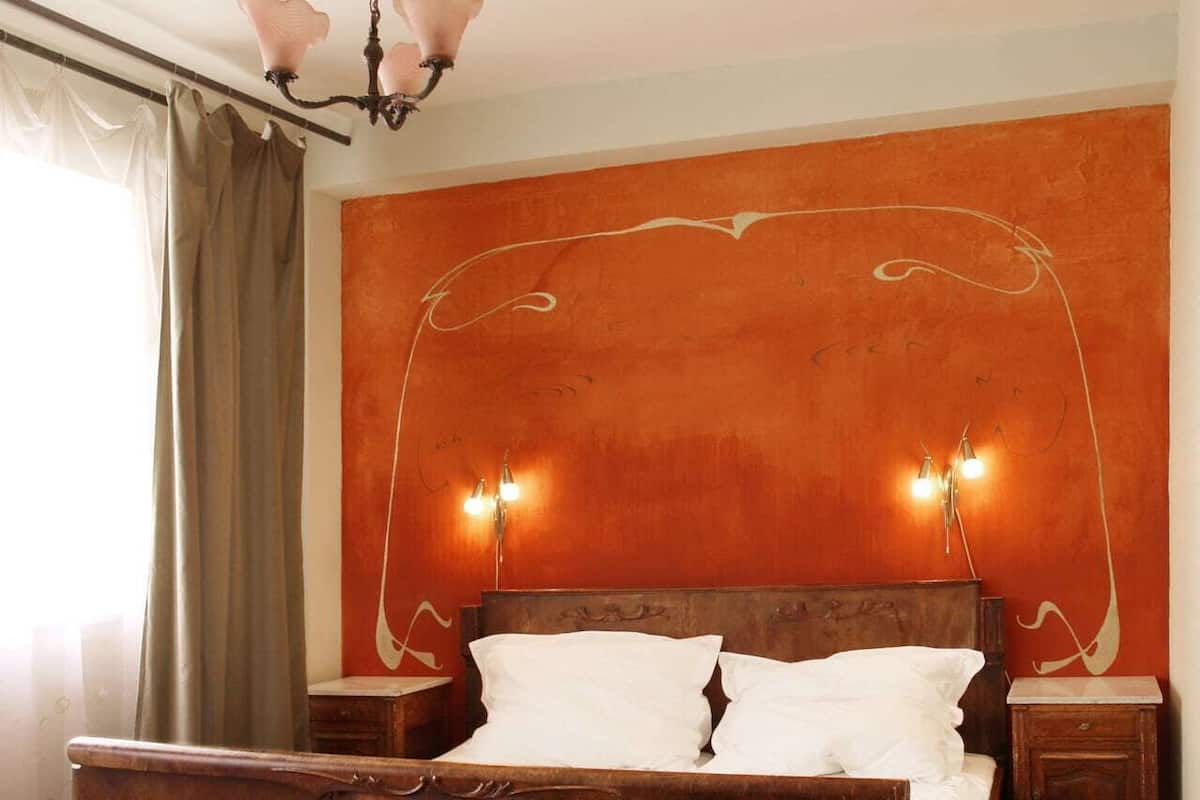 A bedroom with a wooden bed, two bedside tables, a chandelier, and a wall with a decorative design.