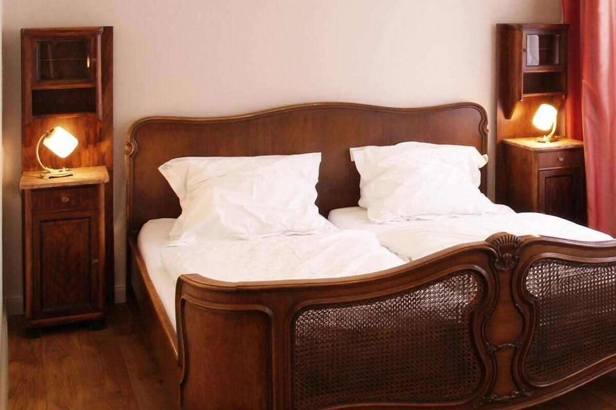 A wooden bed with white linens, two bedside tables with lamps, and a wooden wardrobe.