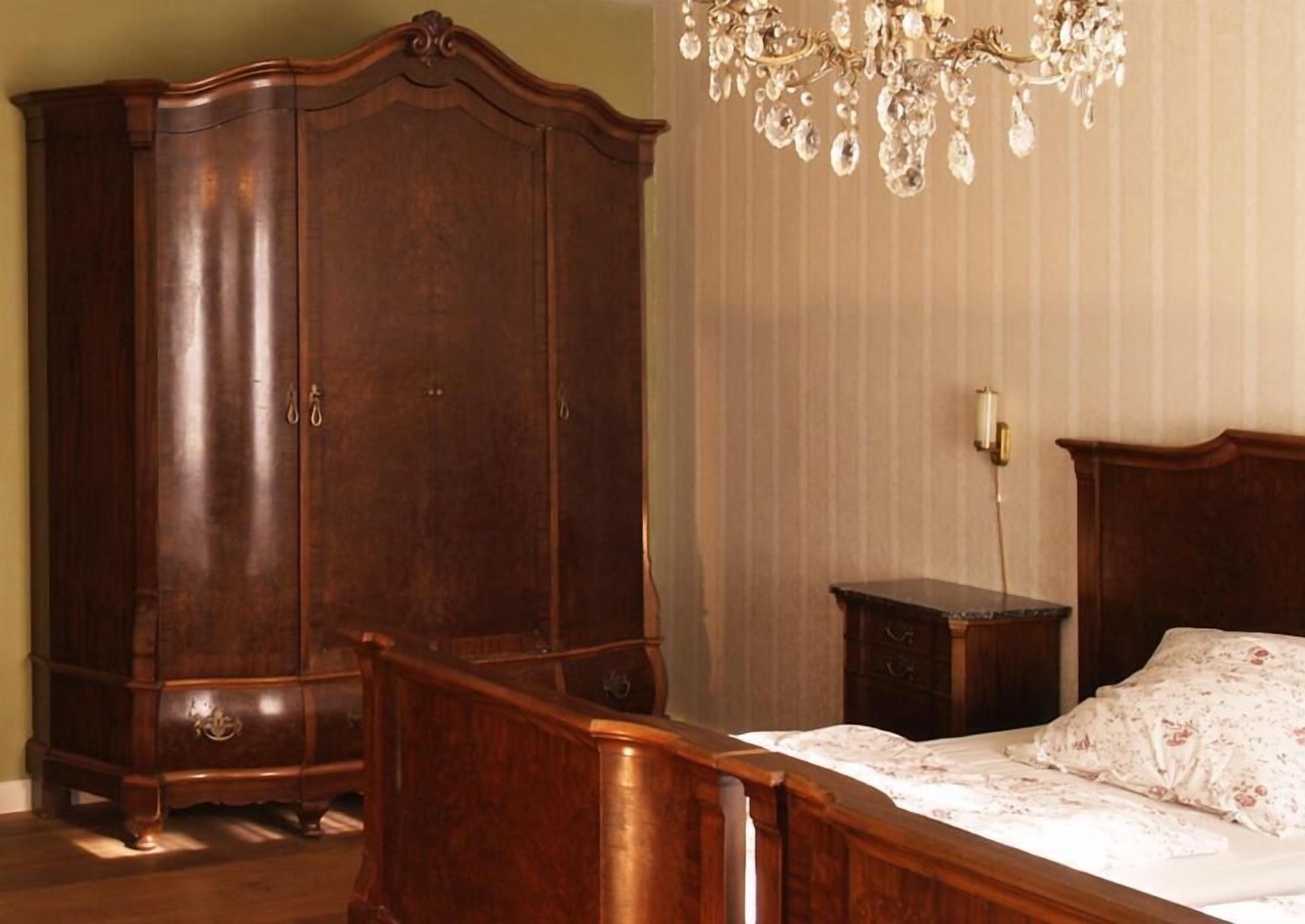 Un dormitorio con un armario de madera grande, una mesita de noche, una cama con ropa de cama floral y una araña.