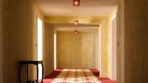 A hallway with a patterned carpet, a table with a chair, and hanging lights. - Hotel Lux (Regensburg)