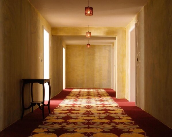 Un pasillo con alfombra estampada, una mesa con una silla y lámparas colgantes.