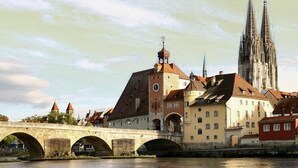 A historic bridge with arches, a clock tower, and a cathedral in the background. - Hotel Lux (Regensburg)