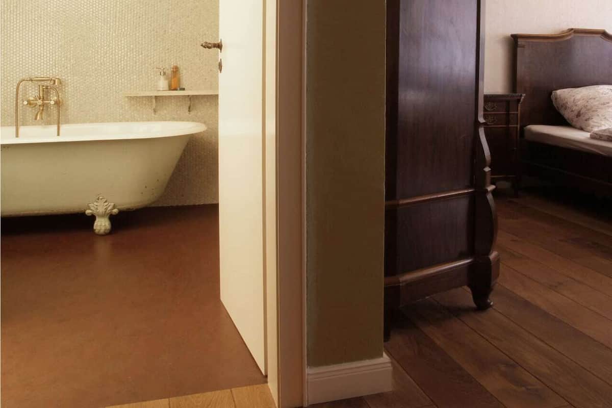 A room with a clawfoot bathtub, a wooden bed, and a wooden floor.