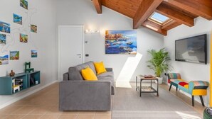 A modern living room with a grey sofa, colorful chairs, a painting of a coastal scene, and a skylight.