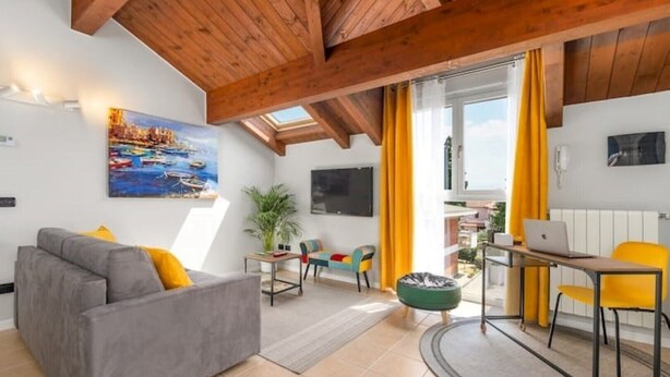 A modern living room with a grey sofa, a green bean bag, and a dining area with yellow chairs.