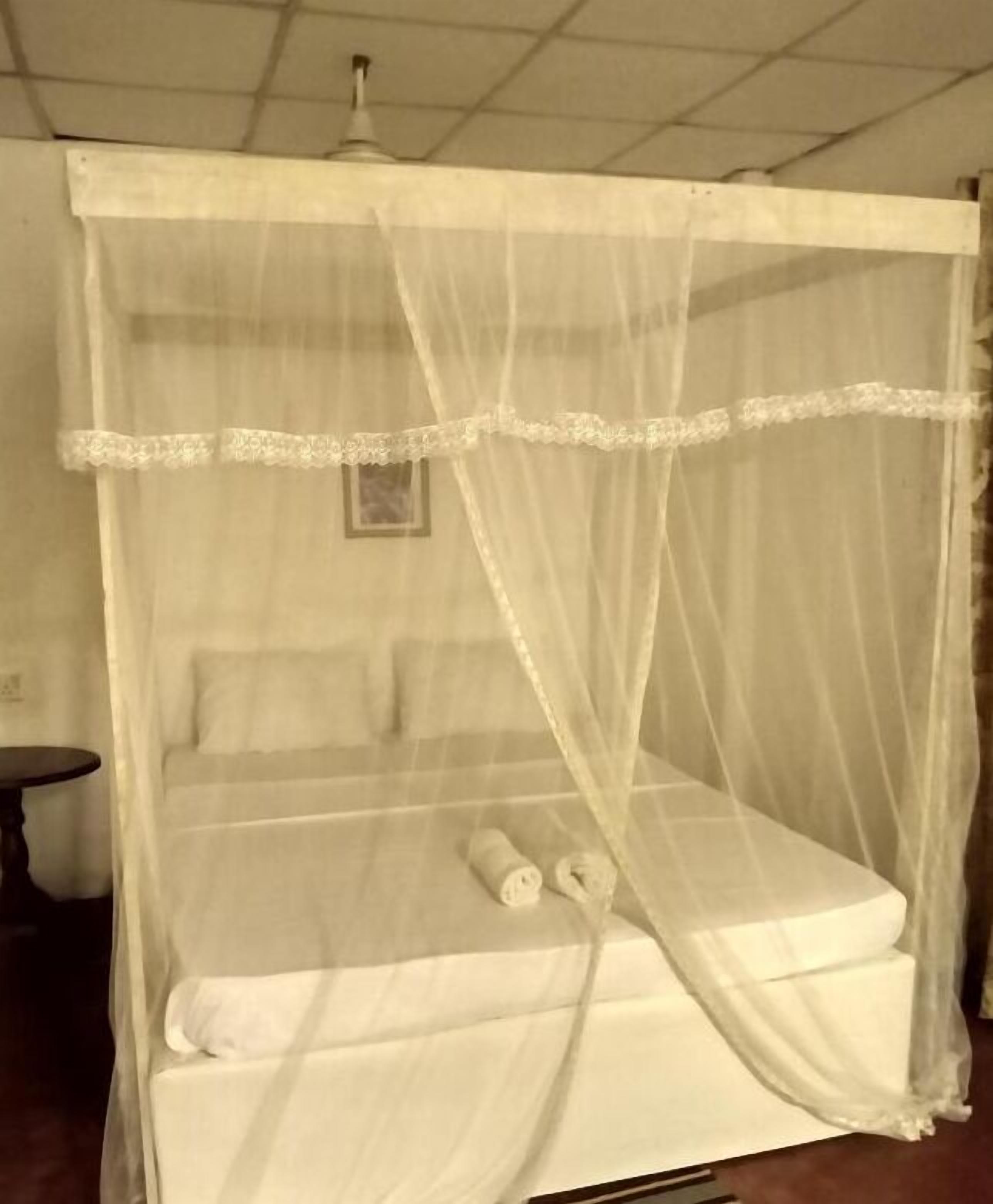 Een bed met hemelbed, kussens en een opgerolde handdoek.
