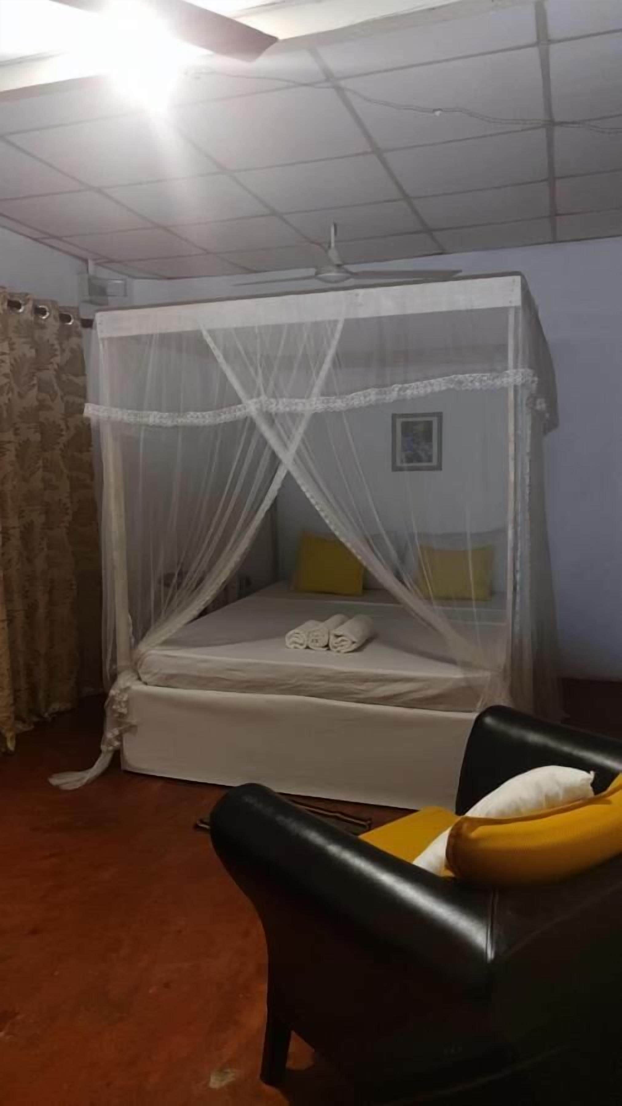 A room with a bed under a canopy, a chair with a cushion, and a ceiling fan.