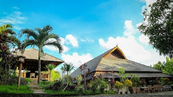 A traditional thatched-roof house with a wooden porch and steps leading up to it, surrounded by lush greenery and palm trees. - Hotel Bukit Indah Saumlaki by LeGreen (Saumlaki)