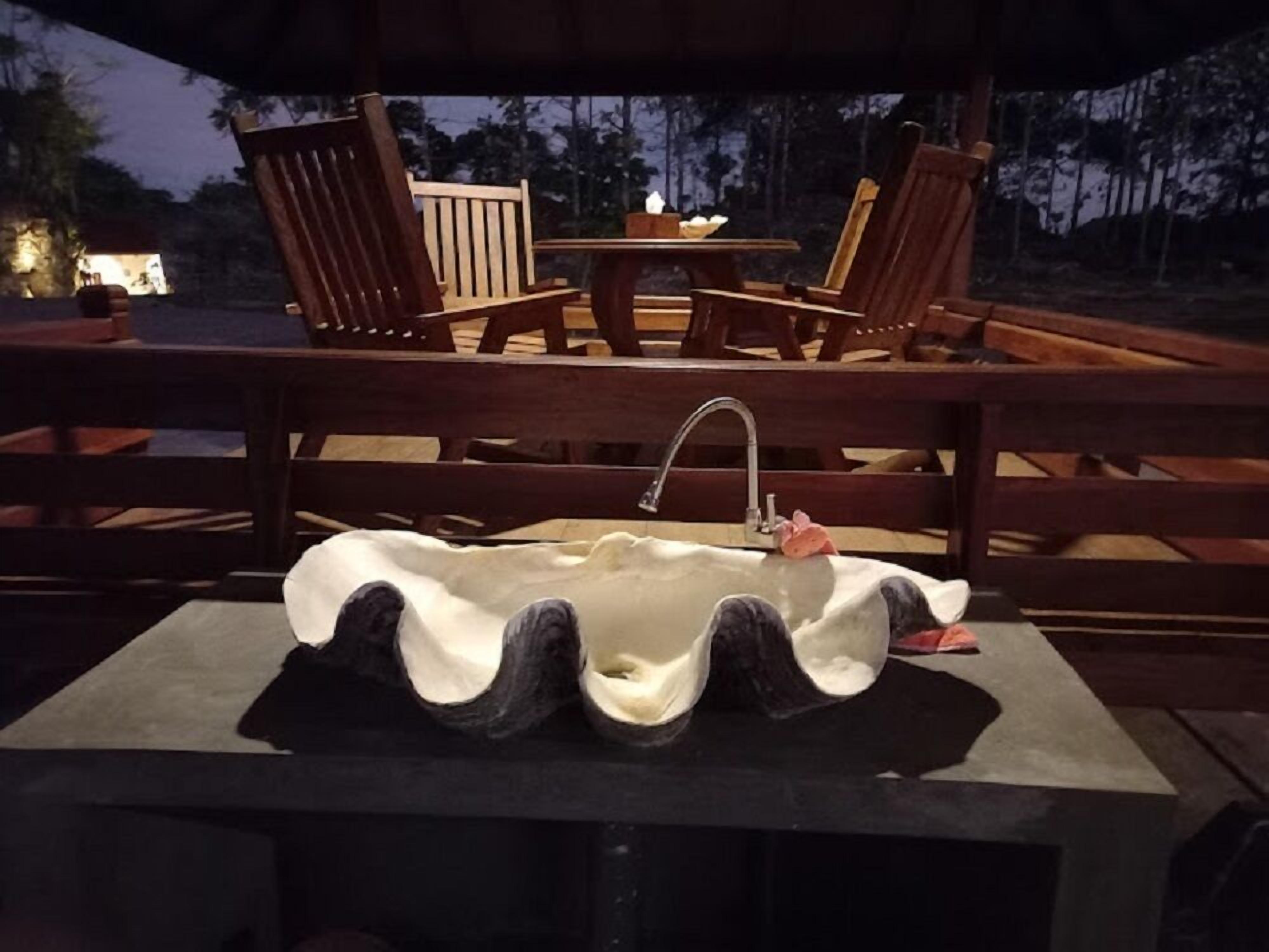 Una terraza de madera con un diseño de lavamanos original, rodeada de sillas y una mesa de madera.