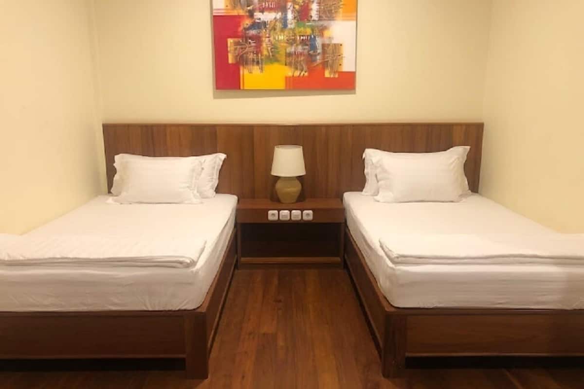 A double room with two single beds, a wooden headboard, a nightstand with a lamp, and a colorful abstract painting on the wall.