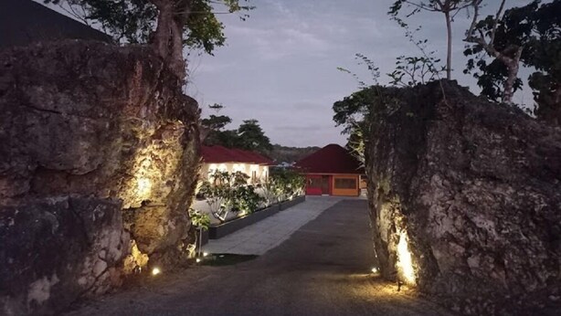 A pathway leading to a building with a red roof, surrounded by stone walls and trees. - Hotel Bukit Indah Saumlaki by LeGreen (Saumlaki)