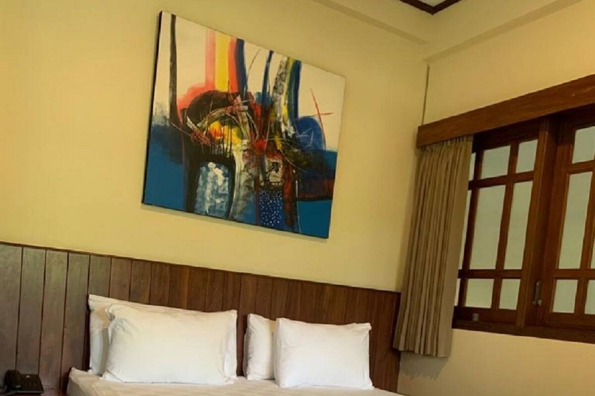 A large bed with a wooden headboard, white bedding, and a nightstand with a phone and a lamp.