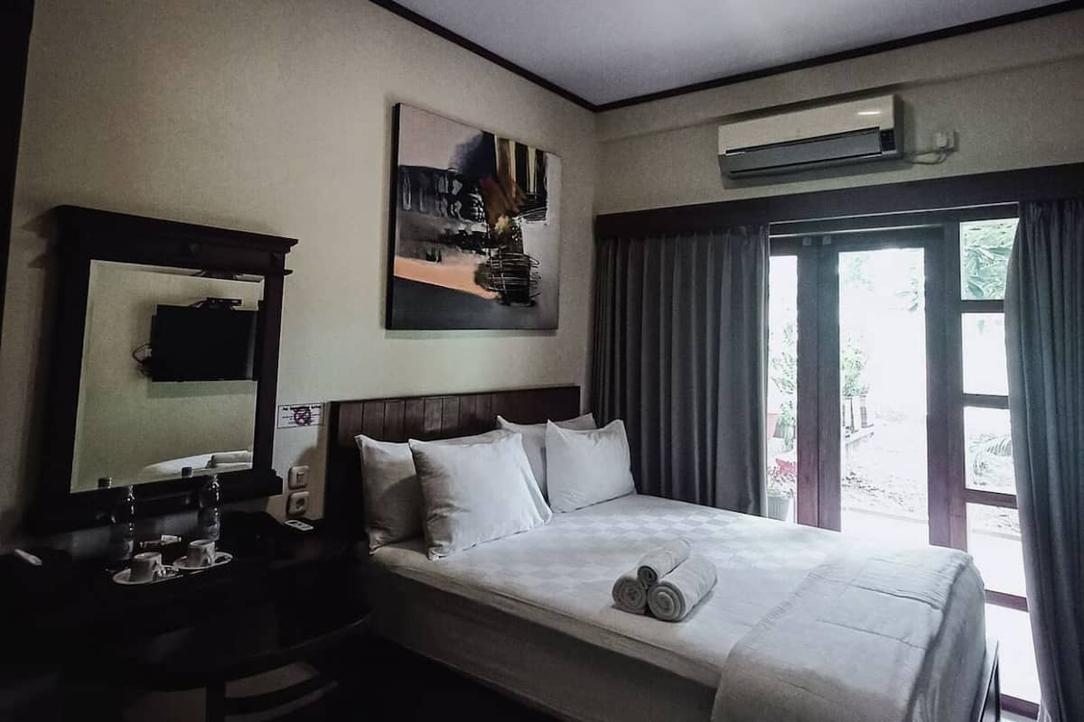 A hotel room with a bed, a desk with a chair, a flat-screen TV, and a painting on the wall.