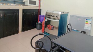 Una cocina con estufa, microondas y refrigerador. Hay una mesa con una silla y una escoba apoyada en la pared.