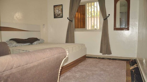 Un dormitorio con una cama, una silla, un ventanal con cortinas, un espejo y un cuadro en la pared.