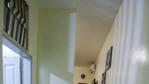 Un pasillo estrecho con una puerta blanca al final, un espejo pequeño en la pared y algunas fotografías.