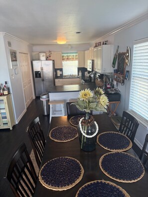 A dining area with a dark wooden table, four chairs, a vase with flowers, and a kitchen in the background.