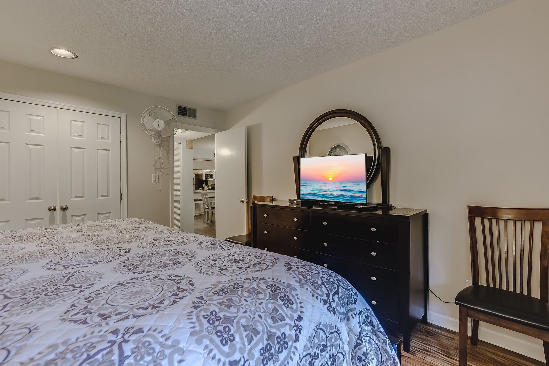 Une chambre à coucher avec un lit, une commode, une chaise et un téléviseur diffusant une image de coucher de soleil.