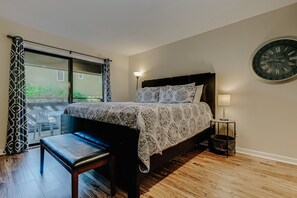 A bedroom with a bed, bench, bedside table, lamp, and a wall clock.