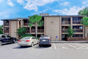 A parking lot with two cars, a multi-story building with balconies, and a blue handicapped parking sign.