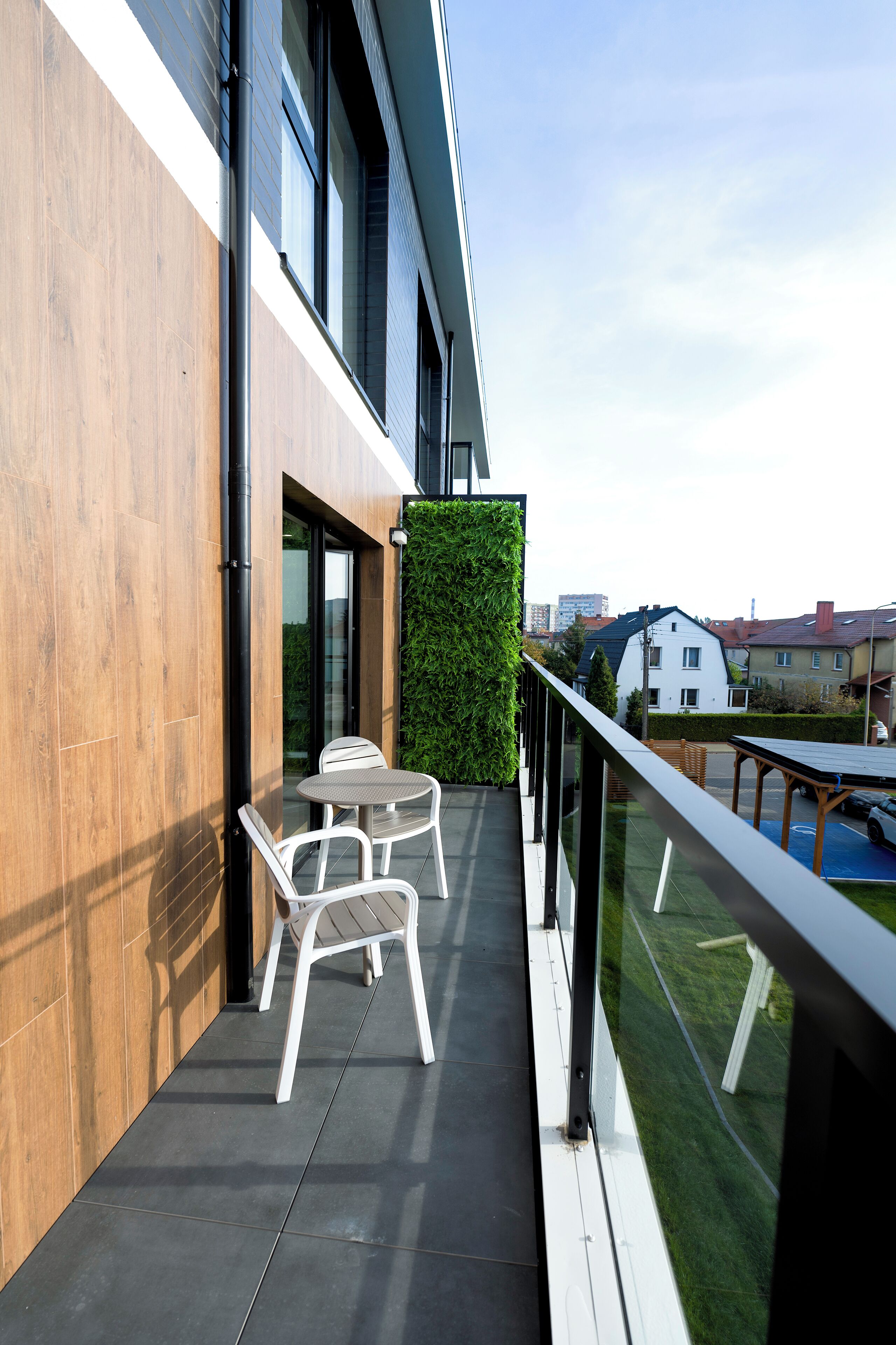 Un balcón con mesa y sillas, un jardín vertical verde y vistas del barrio.