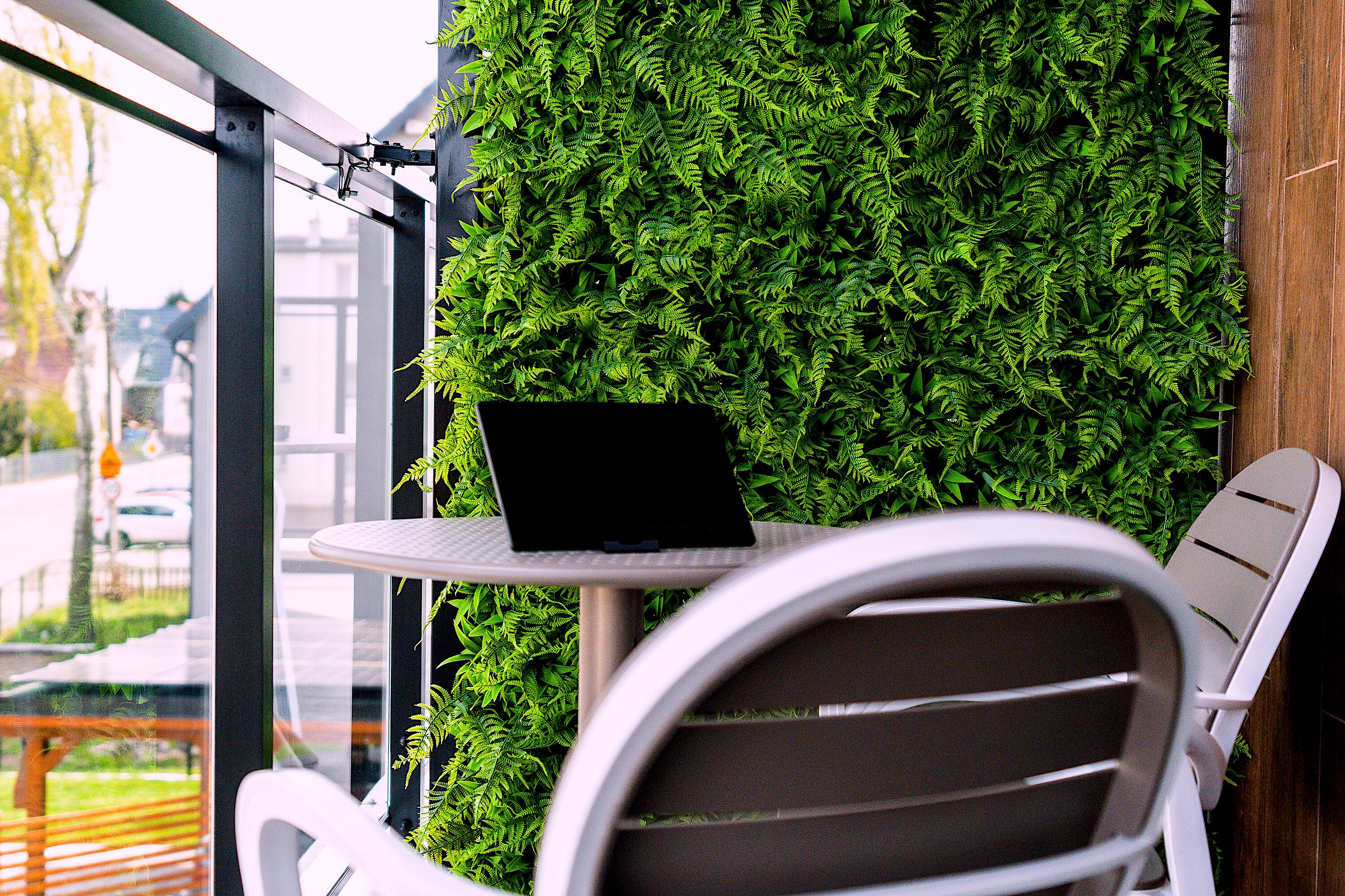 Una mesa con una computadora portátil, una silla y una pared cubierta de follaje verde.