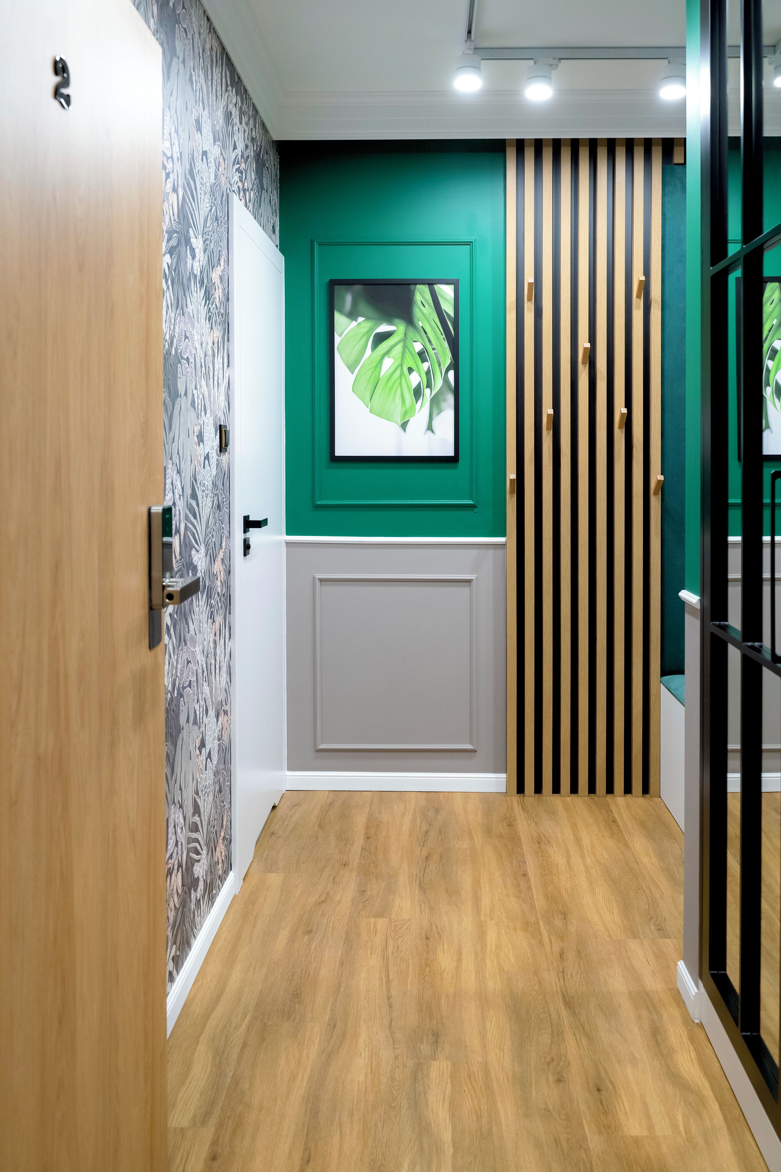 Un pasillo con puerta de madera, pared con diseño, pared de acento verde, un cuadro enmarco y un panel a rayas.
