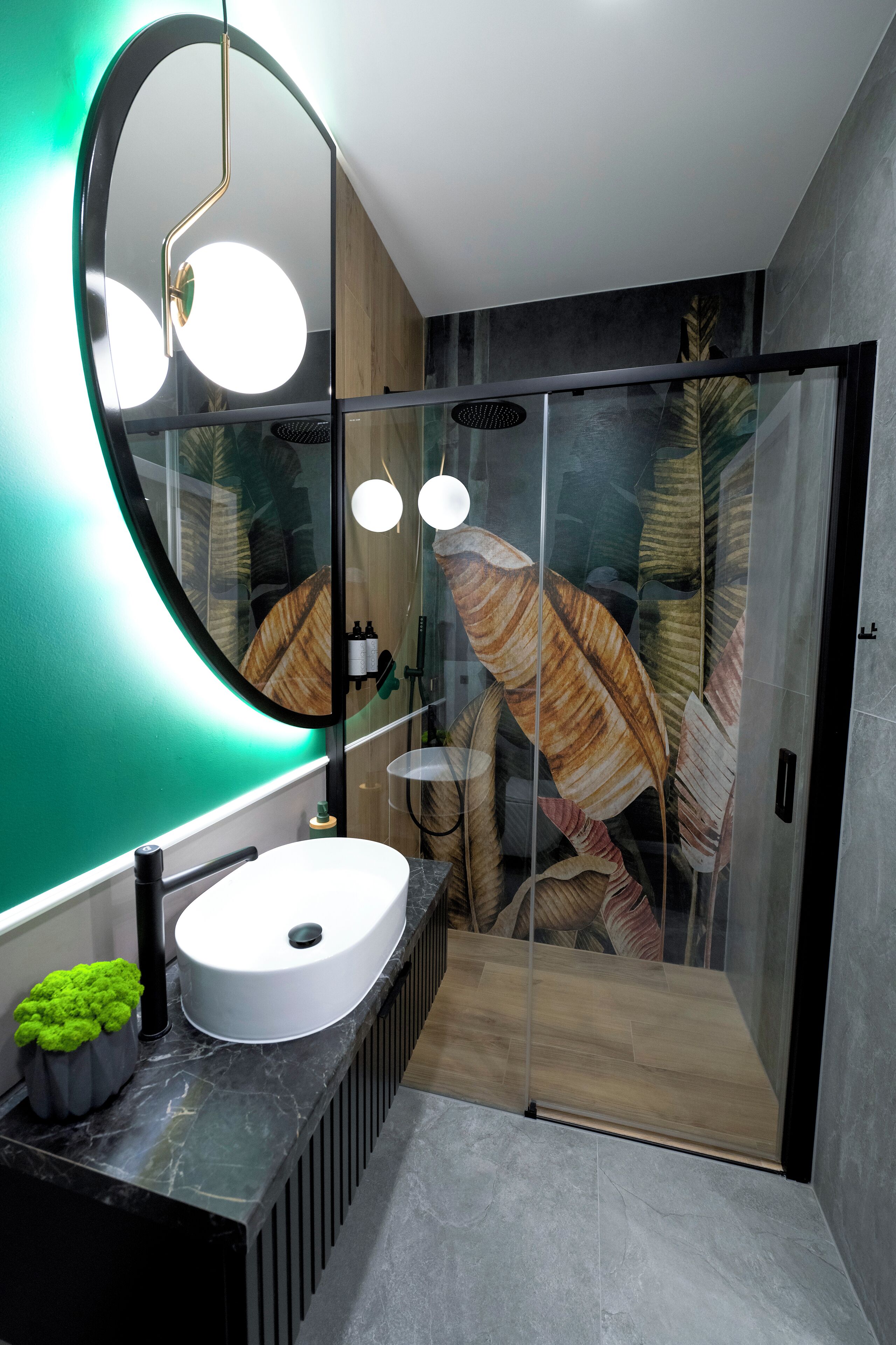 A modern bathroom with a round mirror, a white sink, and a glass shower enclosure.