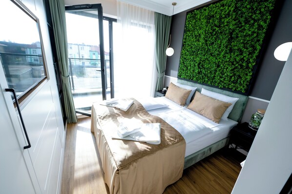 A modern bedroom with a bed, a green wall, a window, and a view of buildings outside. - Aparthotel Green Concrete (Swinoujscie)