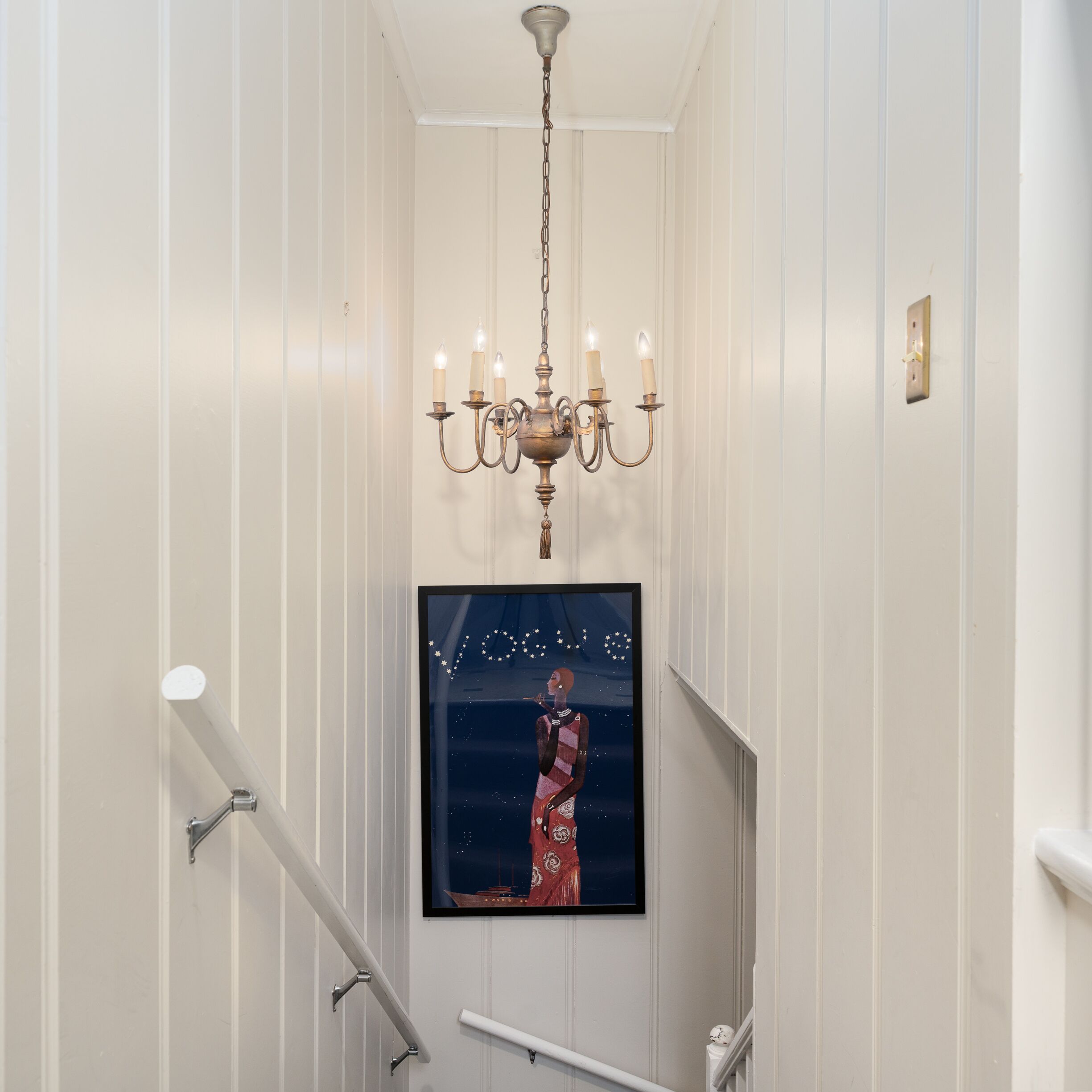 Ein Flur mit einer Chandelier, einem gerahmten Kunstwerk und einer Treppe.