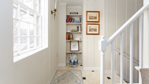 A hallway with a bookshelf, framed pictures, a vase, and a staircase. - Historic 4-Bedroom Home in the Heart of Newport (Newport)