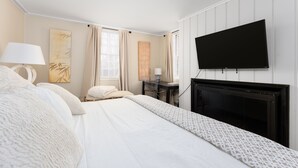 A hotel room with a bed, a flat-screen TV mounted on the wall, a desk with a lamp, and a fireplace. - Historic 4-Bedroom Home in the Heart of Newport (Newport)