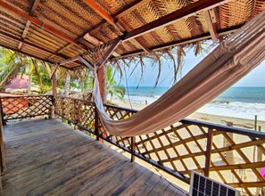 A wooden deck with a hammock, a thatched roof, and a view of the beach and ocean. - Hostal HALALIKU (Santa Marta)