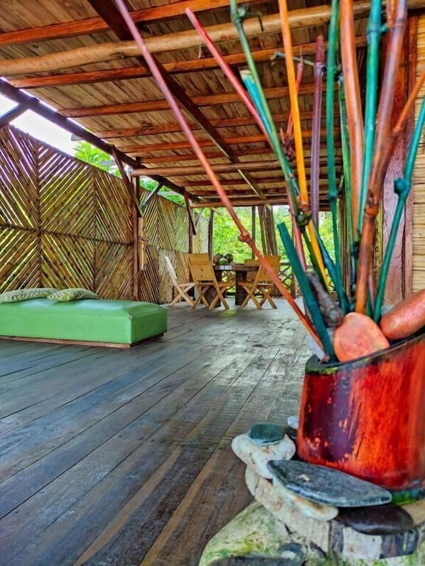 A covered outdoor area with a wooden floor, a green cushioned seating area, and a table with chairs. - Hostal HALALIKU (Santa Marta)