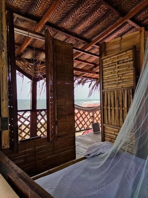 A wooden room with a bed, a mosquito net, and a view of the beach. - Hostal HALALIKU (Santa Marta)