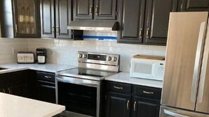 A modern kitchen with dark cabinets, stainless steel appliances, and a wooden floor. - Beautiful Country Setting Near Newport (Portsmouth)