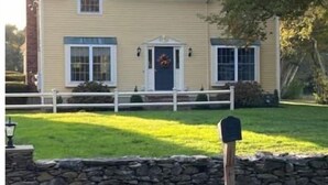A two-story house with a stone wall in front, a mailbox, and a front yard with a lawn and a tree. - Beautiful Country Setting Near Newport (Portsmouth)