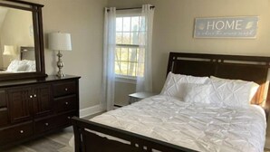 A bedroom with a wooden bed, a dresser, a nightstand, a window with curtains, and a wall sign that says "HOME". - Beautiful Country Setting Near Newport (Portsmouth)