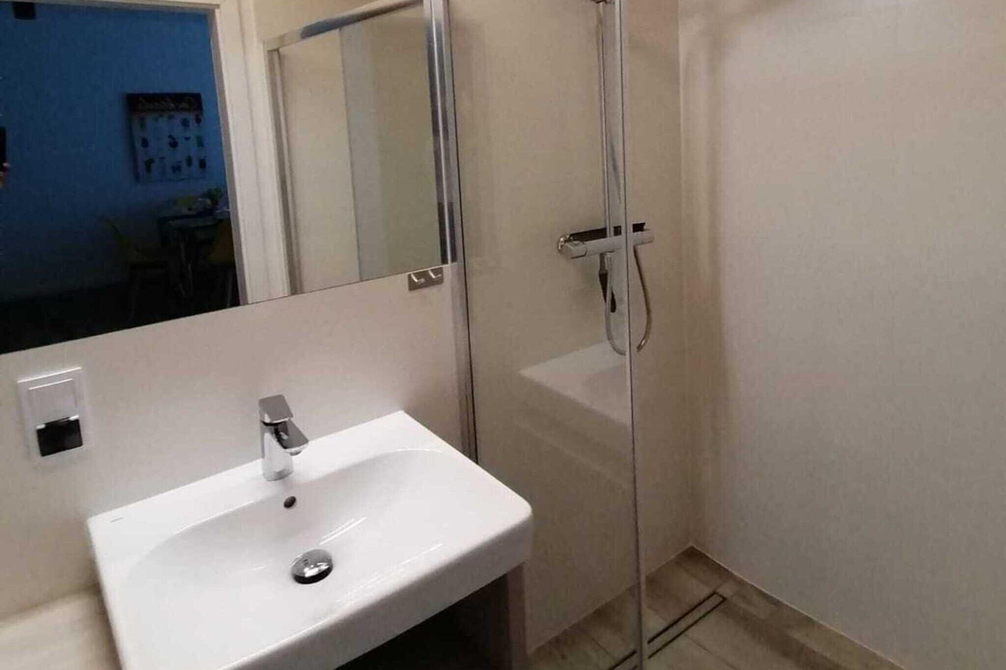 Een badkamer met een wit wastafel, een spiegel en een douche.