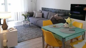Una sala de estar moderna con un sofá, una mesa de comedor con sillas amarillas, una pequeña mesita auxiliar y un florero con flores.