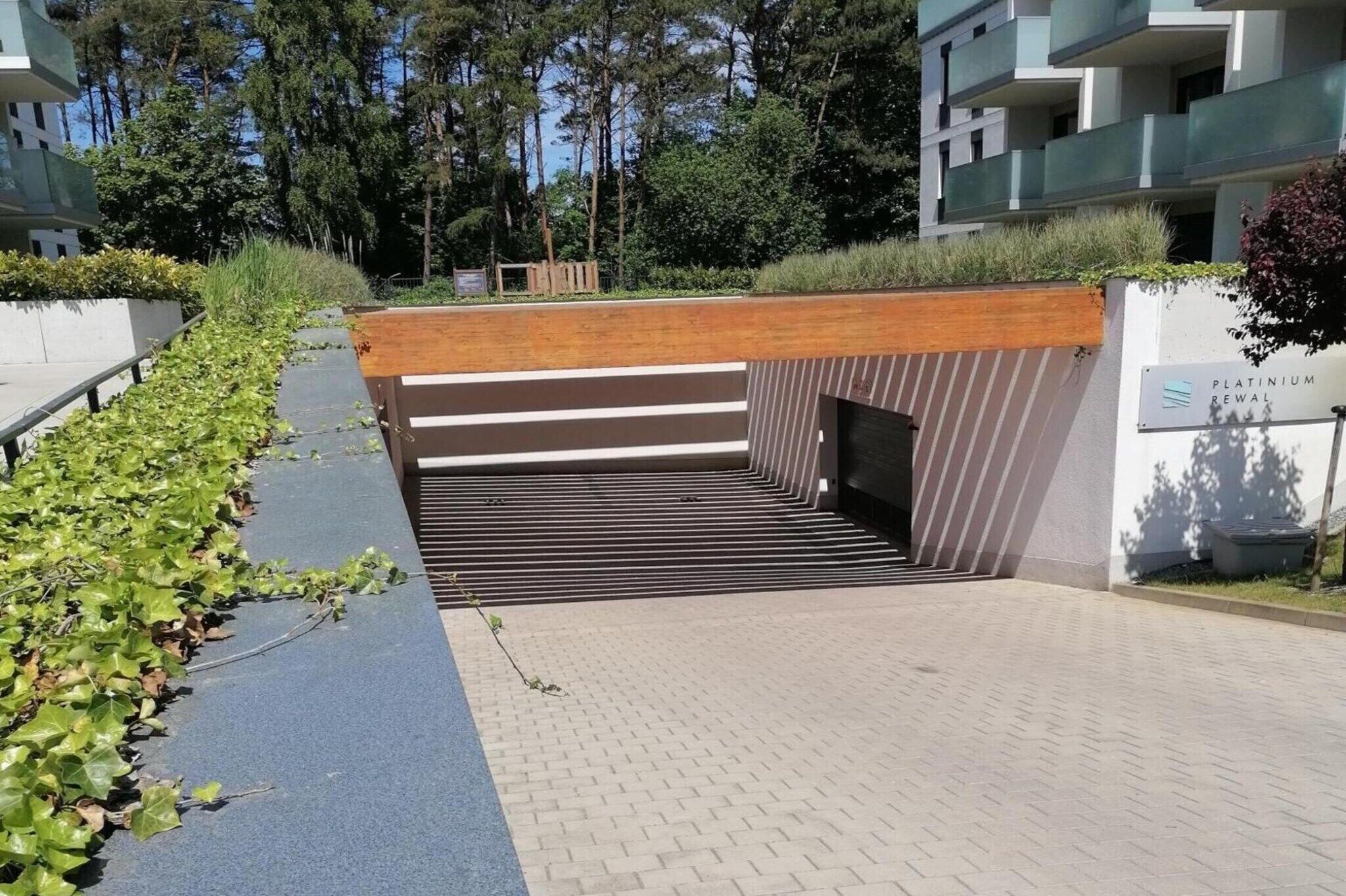 A modern building entrance with a wooden overhang, a paved pathway, and a sign for 'Platinum Rewal'.
