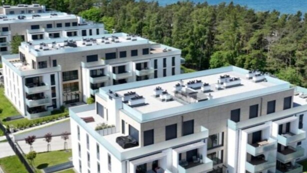 Un moderno complejo de apartamentos con varios edificios, cada uno con balcones y una azotea plana con unidades de aire acondicionado.