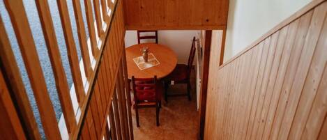 Un escalier en bois mène à un espace repas où se trouvent une table ronde et des chaises.