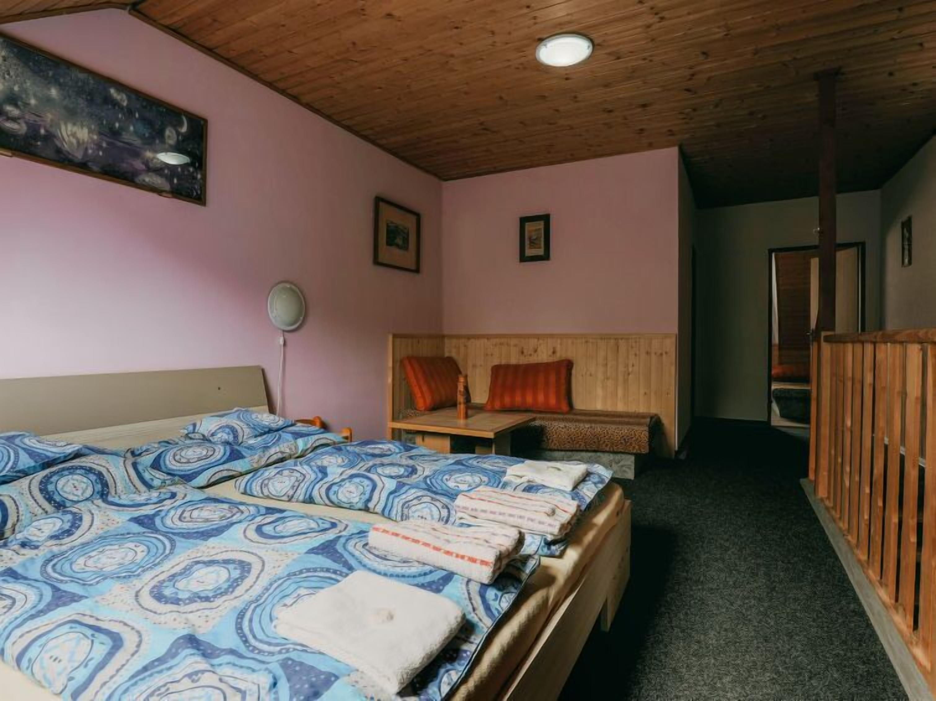 Una stanza con soffitto in legno, un letto con lenzuola a motivi, una panca con cuscini e un quadro appeso al muro.