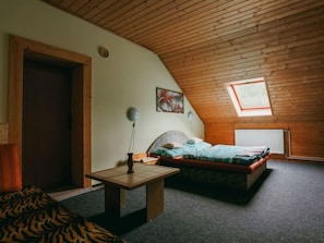 A cozy bedroom with a sloped ceiling, a single bed, a small table, and a window with a view.